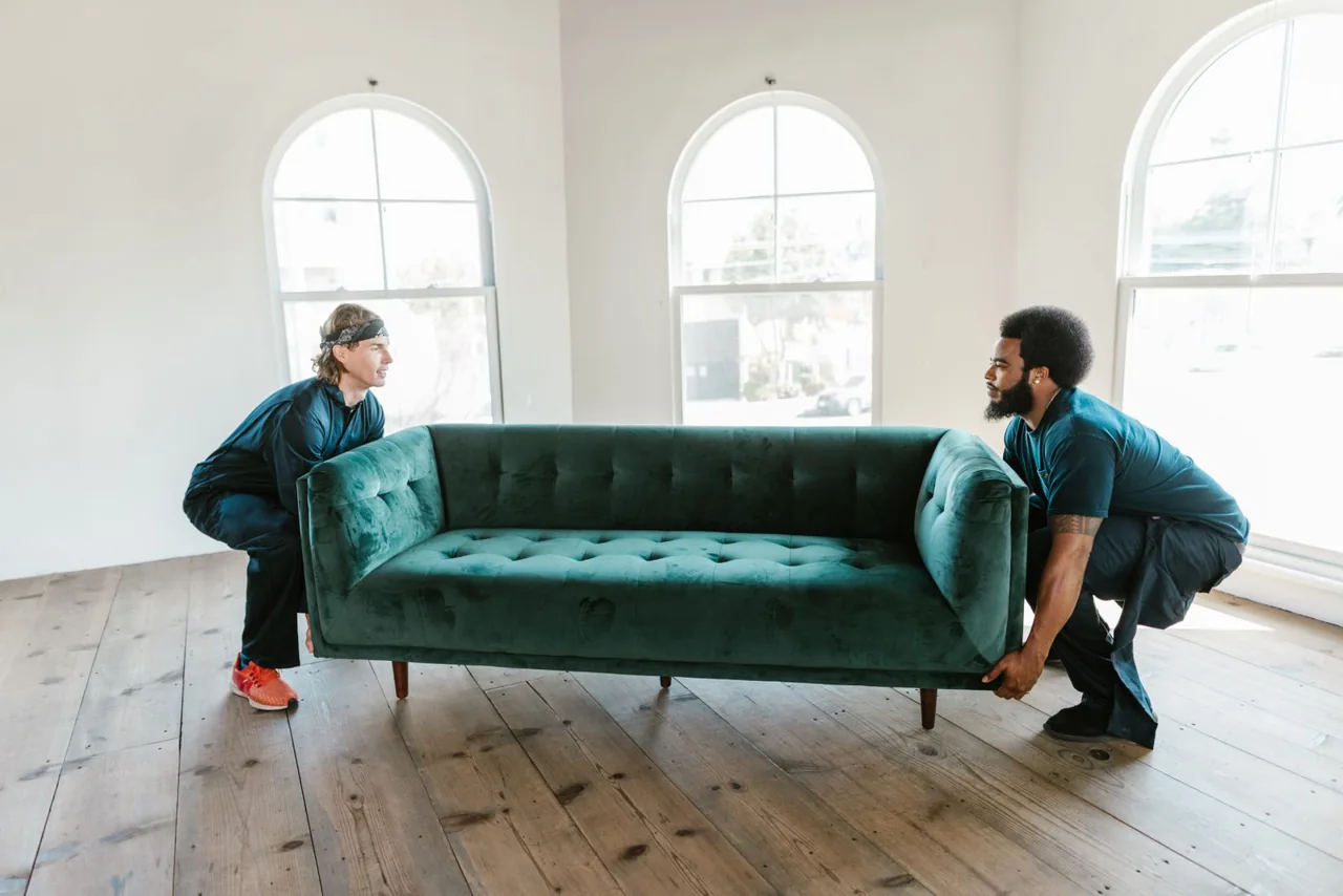 Two workers lifting a sofa together in a sunlit room. Illustrative stock photograph.