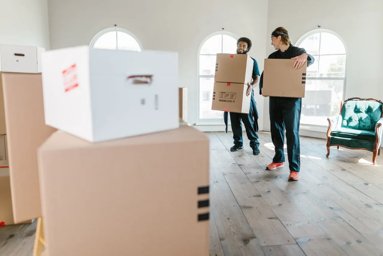 Two workers carrying cardboard boxes inside a property. Illustrative stock photograph.